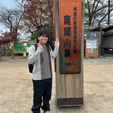 高尾山の山頂で標識の横に立っているところ