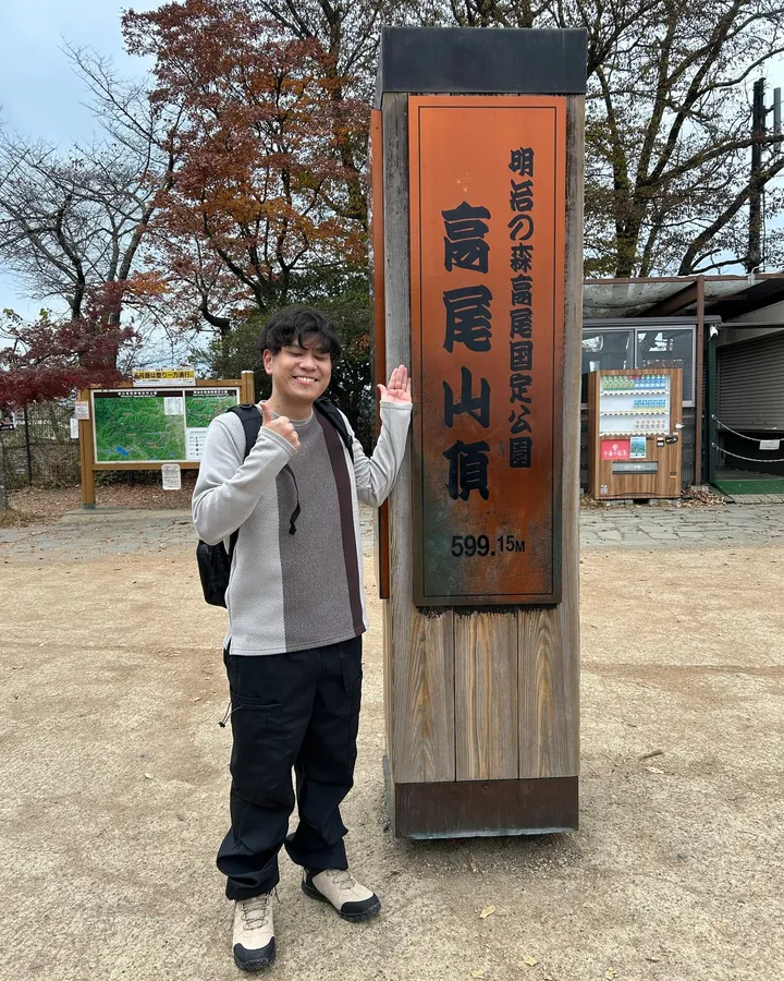 高尾山の山頂で標識の横に立っているところ