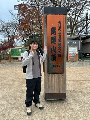 高尾山の山頂で標識の横に立っているところ